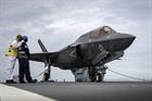 An aircraft handler receives instructions with the F-35 strapped to the deck